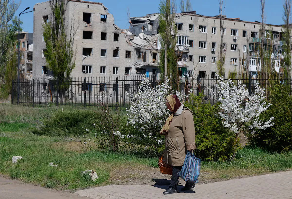 Жінка виходить із церкви під час святкування православного Великодня, а на задньому плані видно житловий будинок, пошкоджений під час російсько-українського конфлікту, в Авдіївці (Авдіївка), Донецька область, контрольована Росією територія України, 20 кві